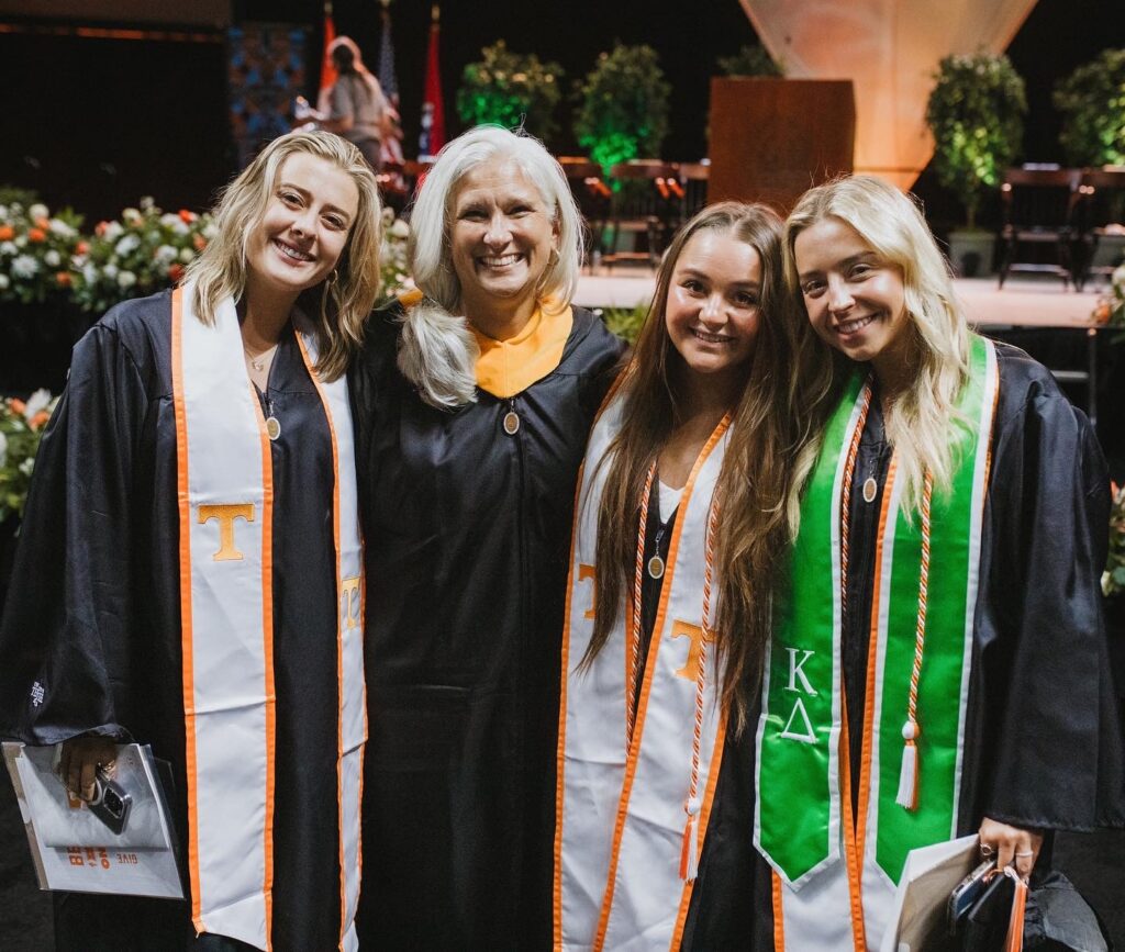 Jules with three graduates in UT stoles in front of the commencement stage