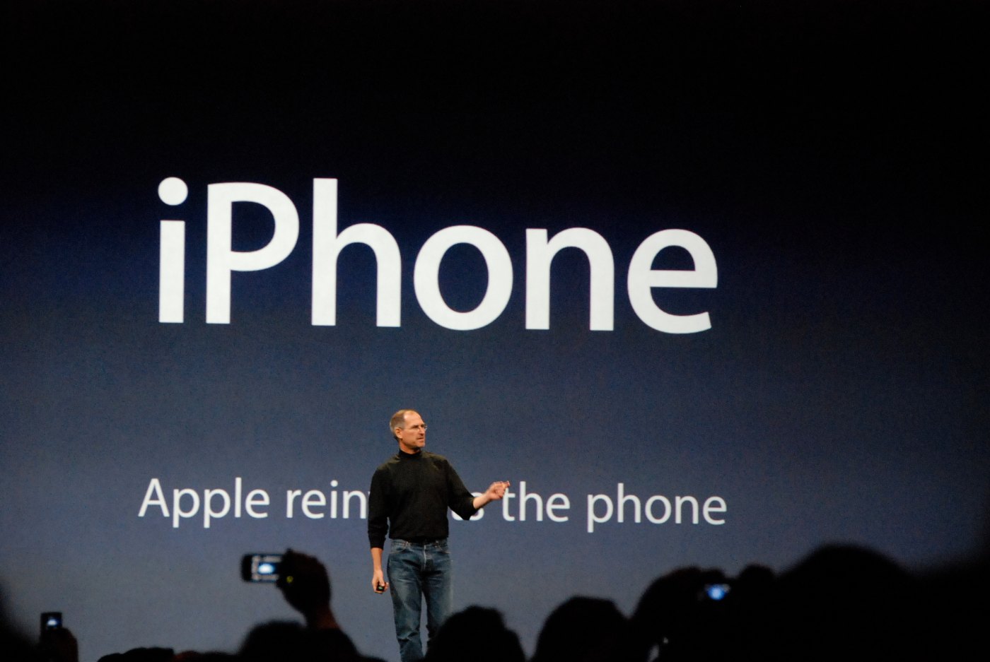 Steve Jobs on stage in 2007 in front of a slide reading Apple reinvents the phone