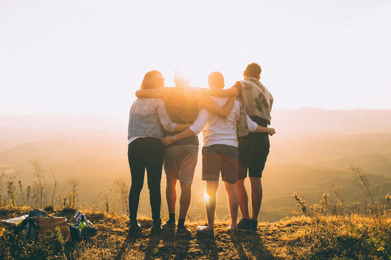 Friends with arms around each other watching a sunset