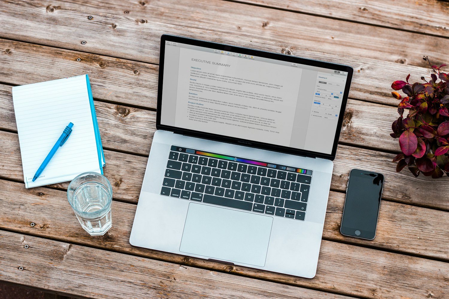 A notebook and pen beside a laptop on a writing desk