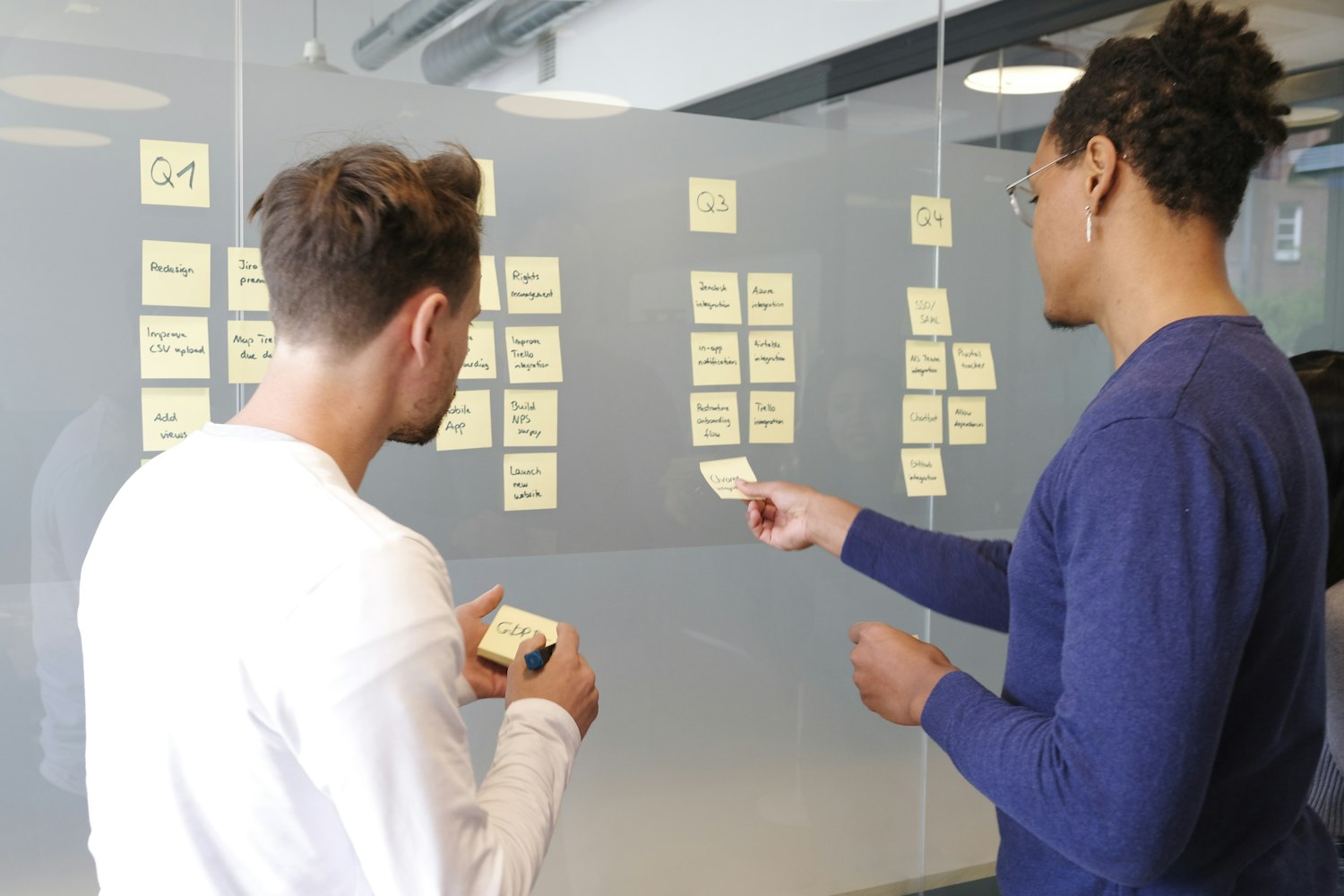 Two teammates planning a project with sticky notes on a glass wall
