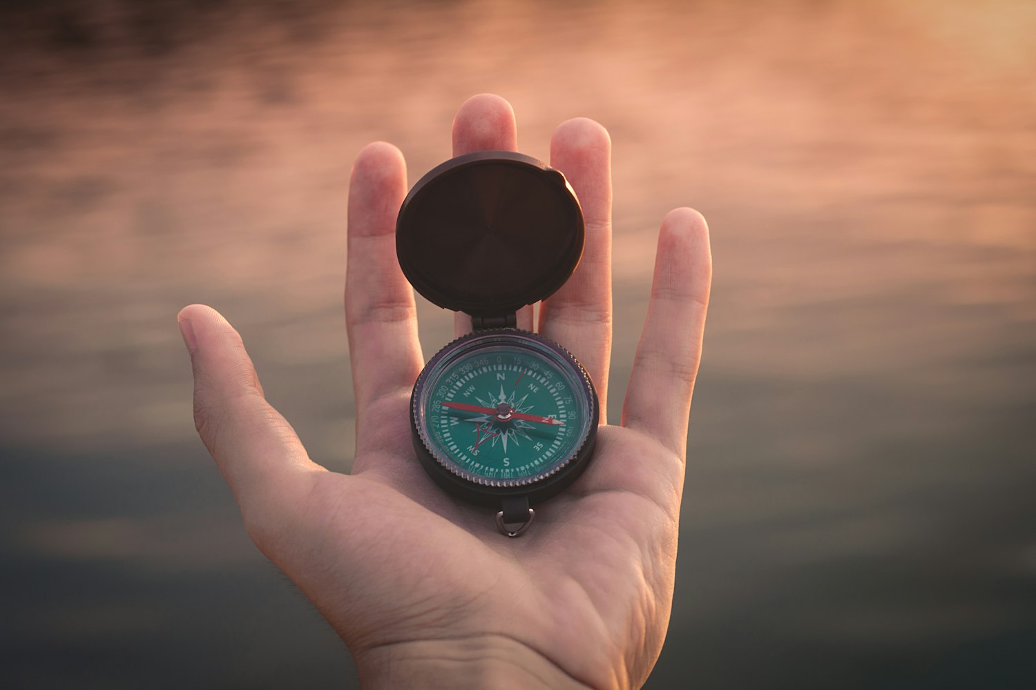 A hand holding a compass outdoors
