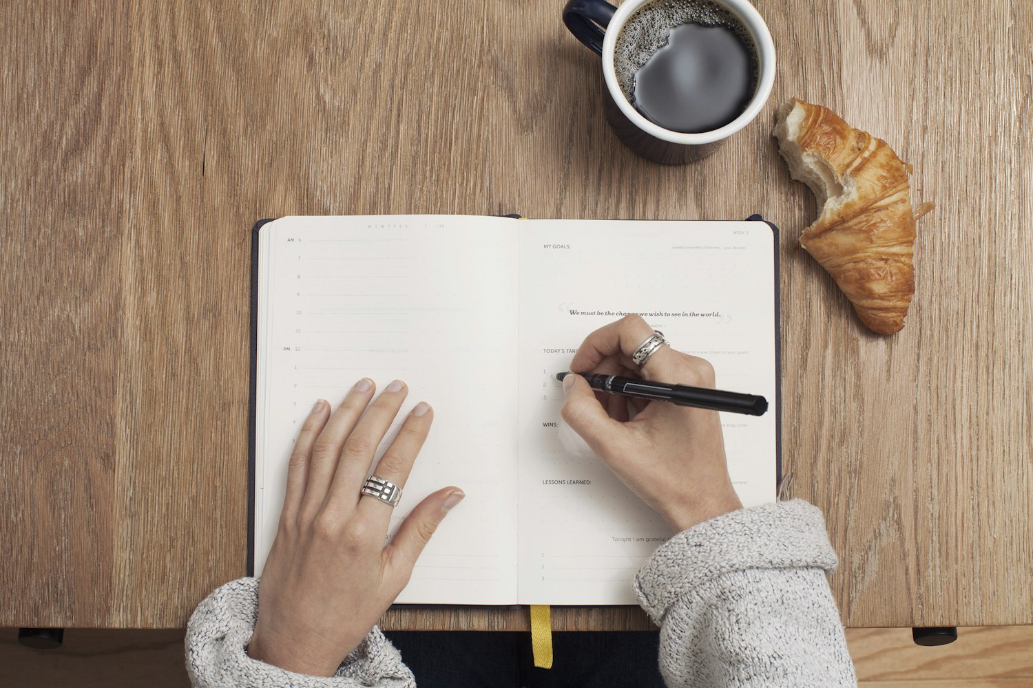 A person writing in a journal next to a cup of coffee