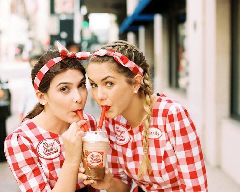 Two women in red gingham and bandanas sharing a Cruze Farm drink