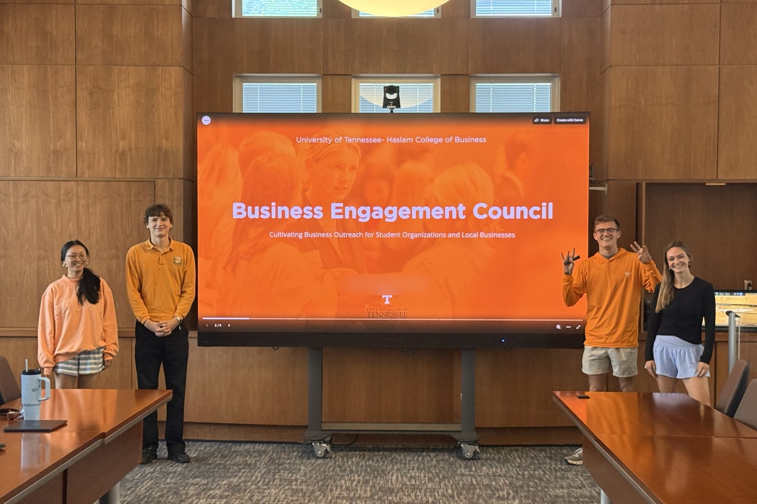 A BUAD 497 student team stands beside its Business Engagement Council title slide while presenting in a Haslam classroom