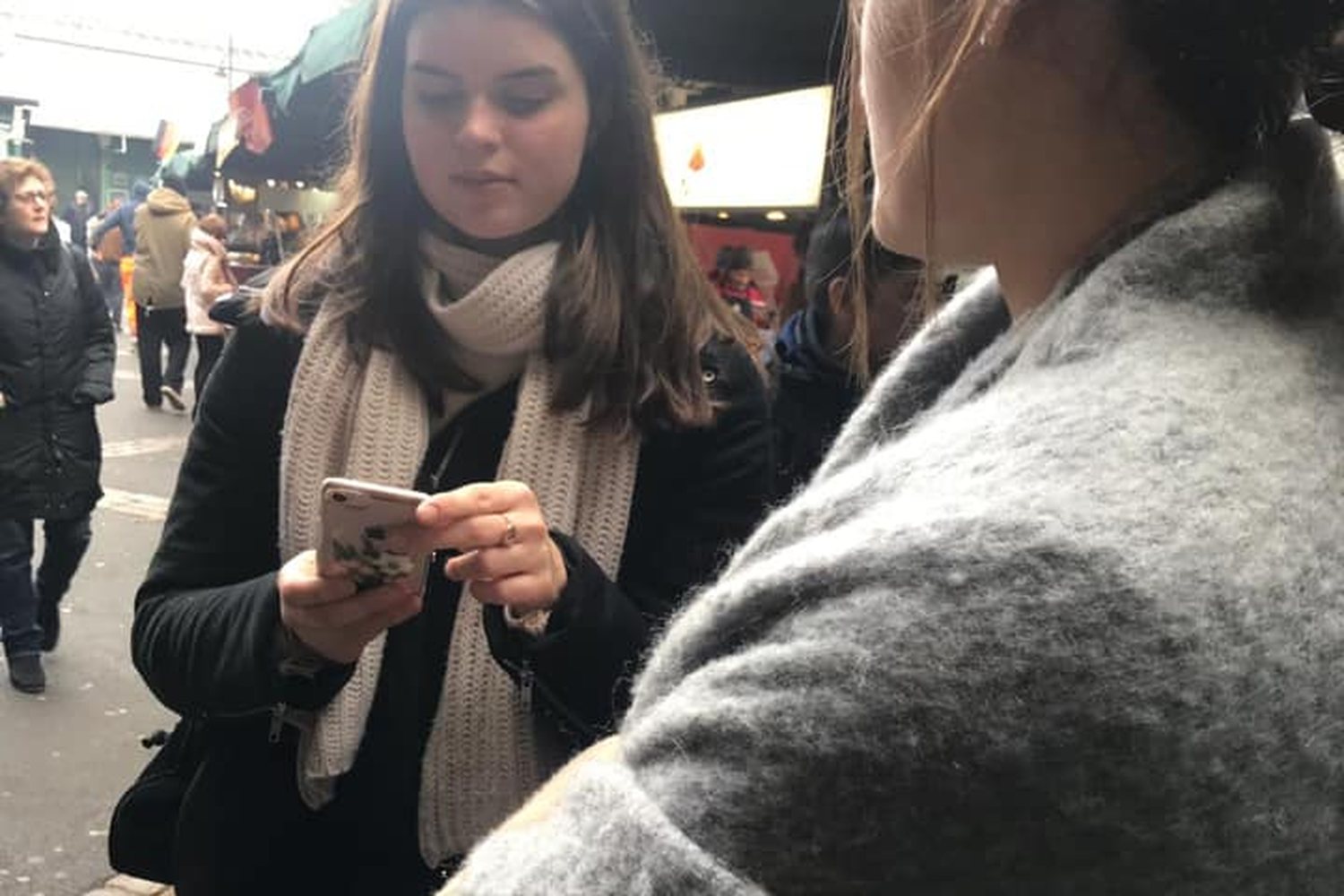 A student checks her phone while talking with a classmate on a busy London street