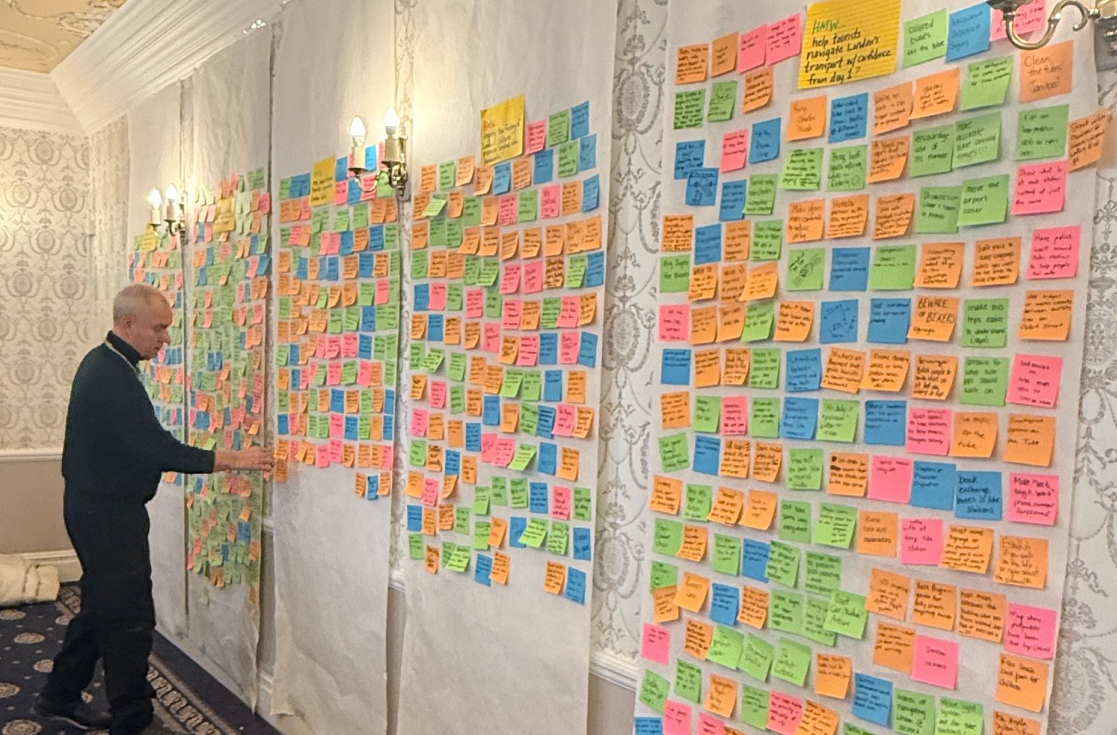 Lane Morris adding a sticky note to a long wall of brainstorm ideas