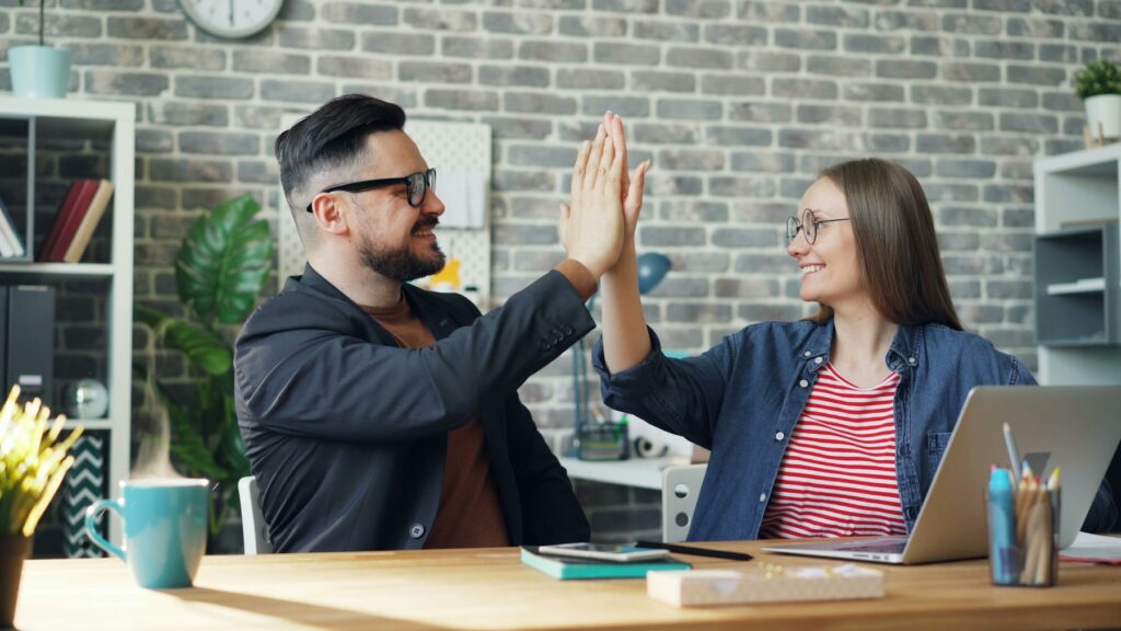 Two coworkers at a table giving each other a high five