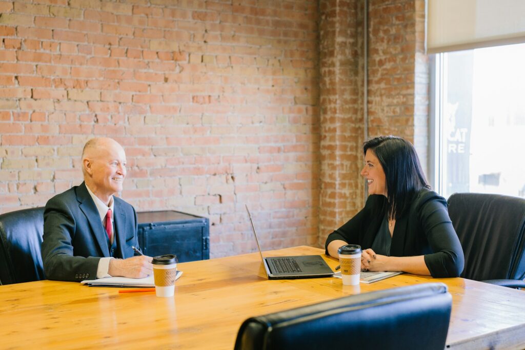 Senior executive and a colleague talking across a table, notes and laptop open