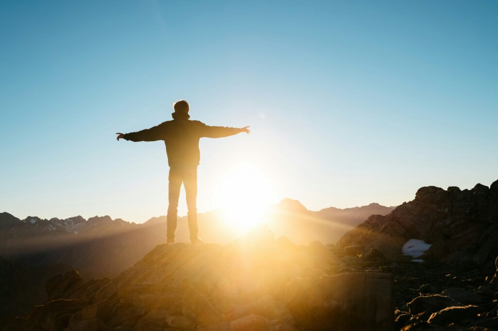 A person with arms wide open facing the sunrise on a mountain
