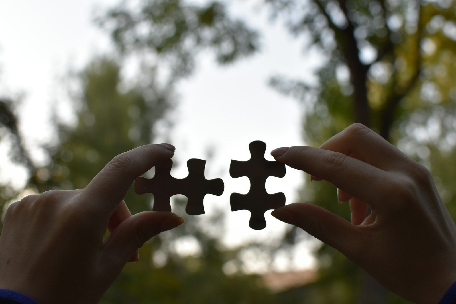 Two hands holding two puzzle pieces about to fit together