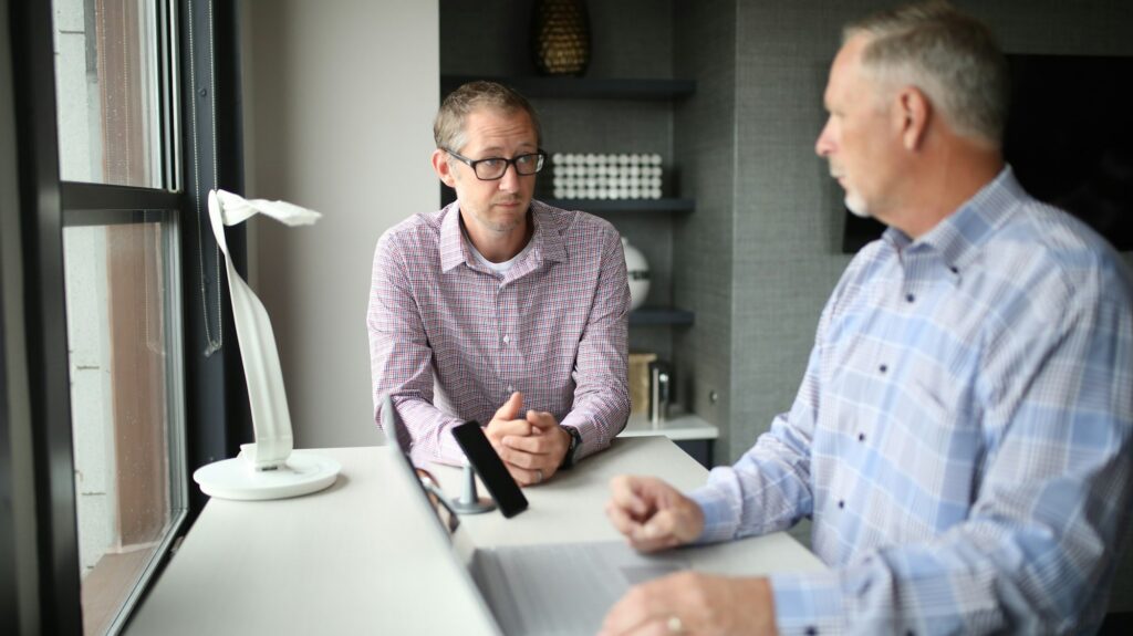 An older manager coaching a younger colleague at his desk