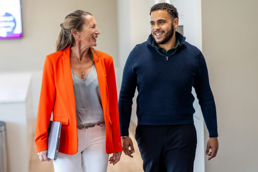 A woman and a younger male colleague talking as they walk through the office