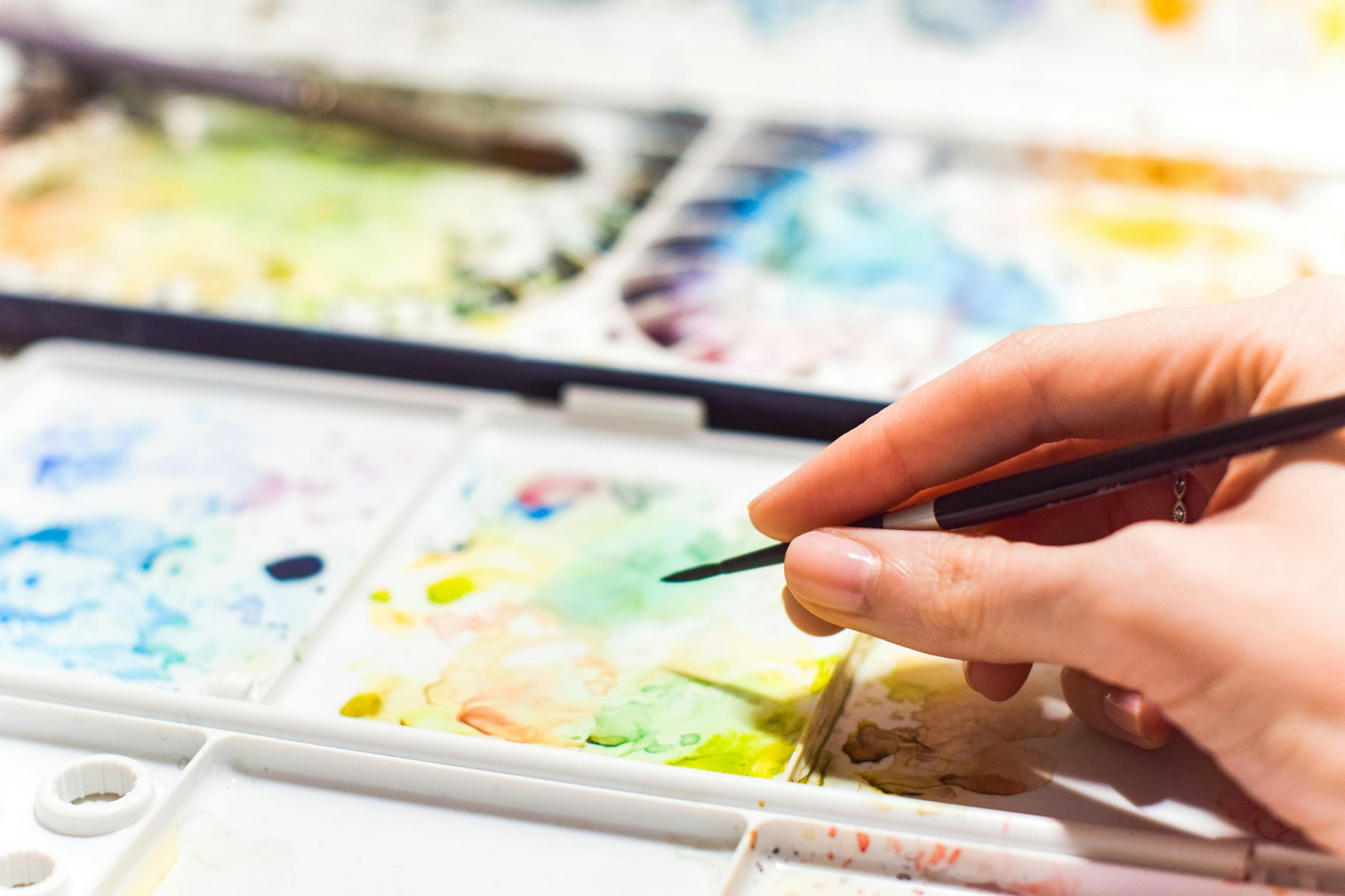 A hand painting with watercolors at a table covered in color