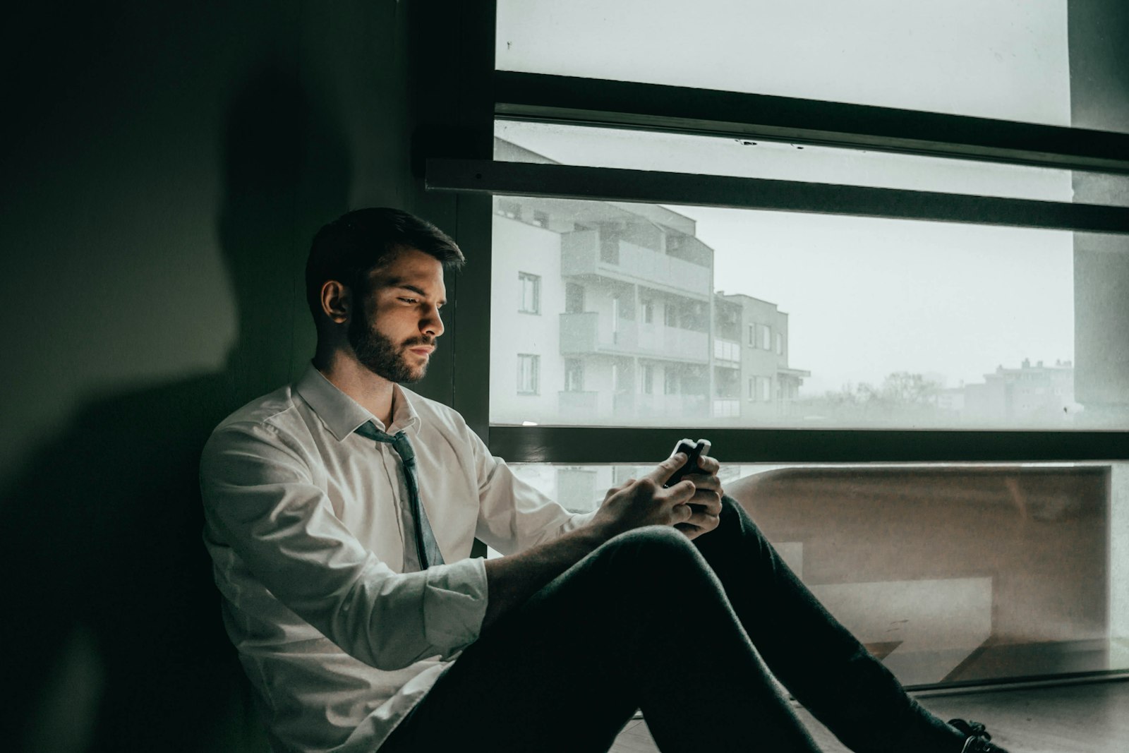 A man in a shirt and tie sitting by an office window, deep in thought