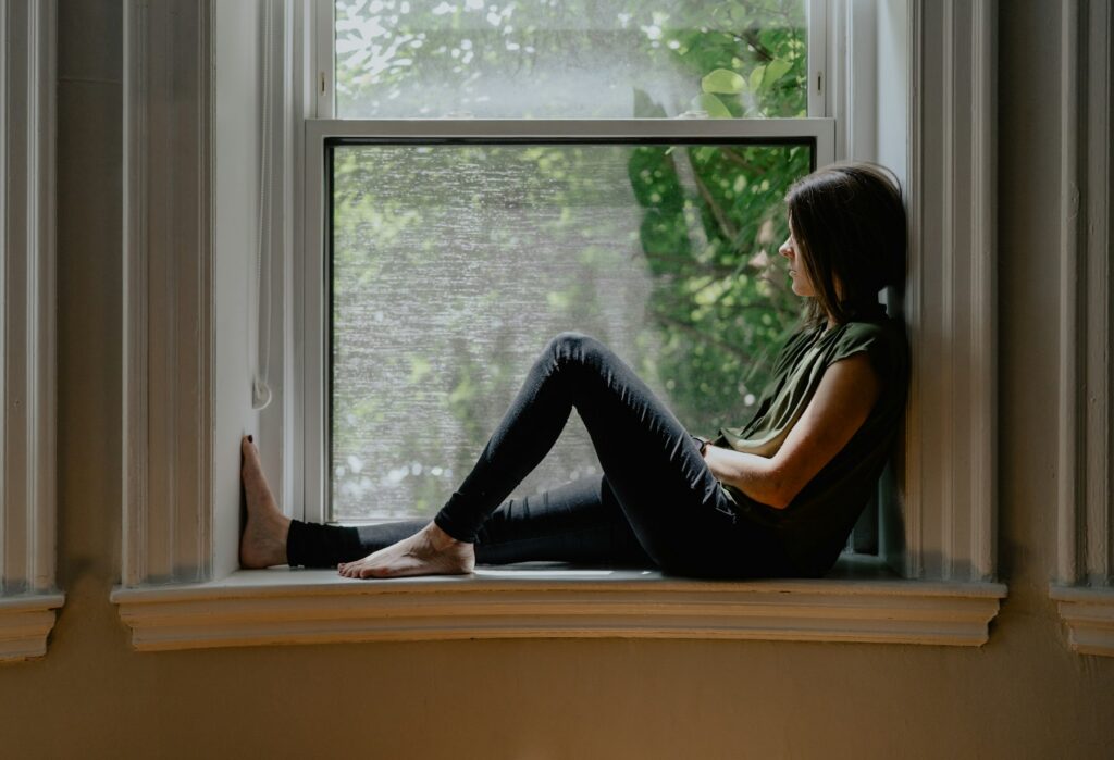 A woman sitting on a window sill, lost in thought