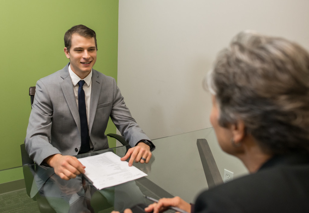 A young man in a suit sitting across a desk from an interviewer