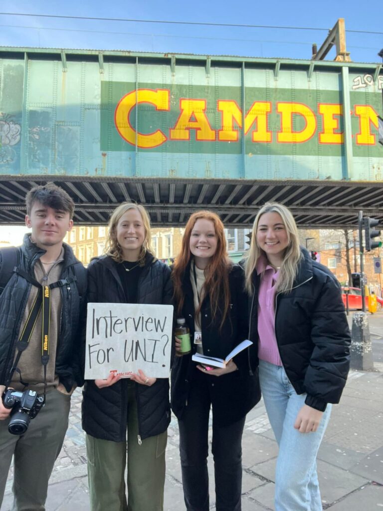 Students holding an "Interview me" sign under the Camden Market sign in London