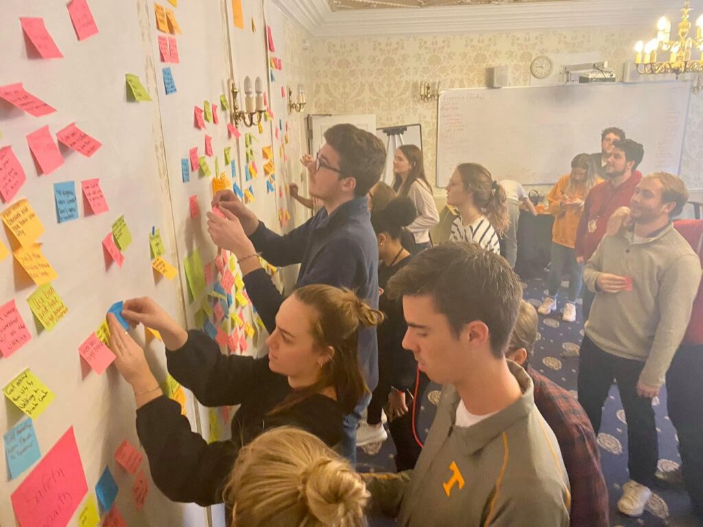 A crowd of students adds sticky notes to a long wall as they cluster ideas