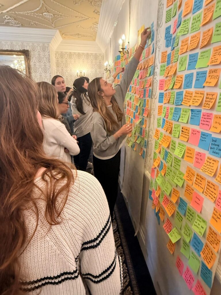 Students crowd a wall covered floor to ceiling in colorful idea notes