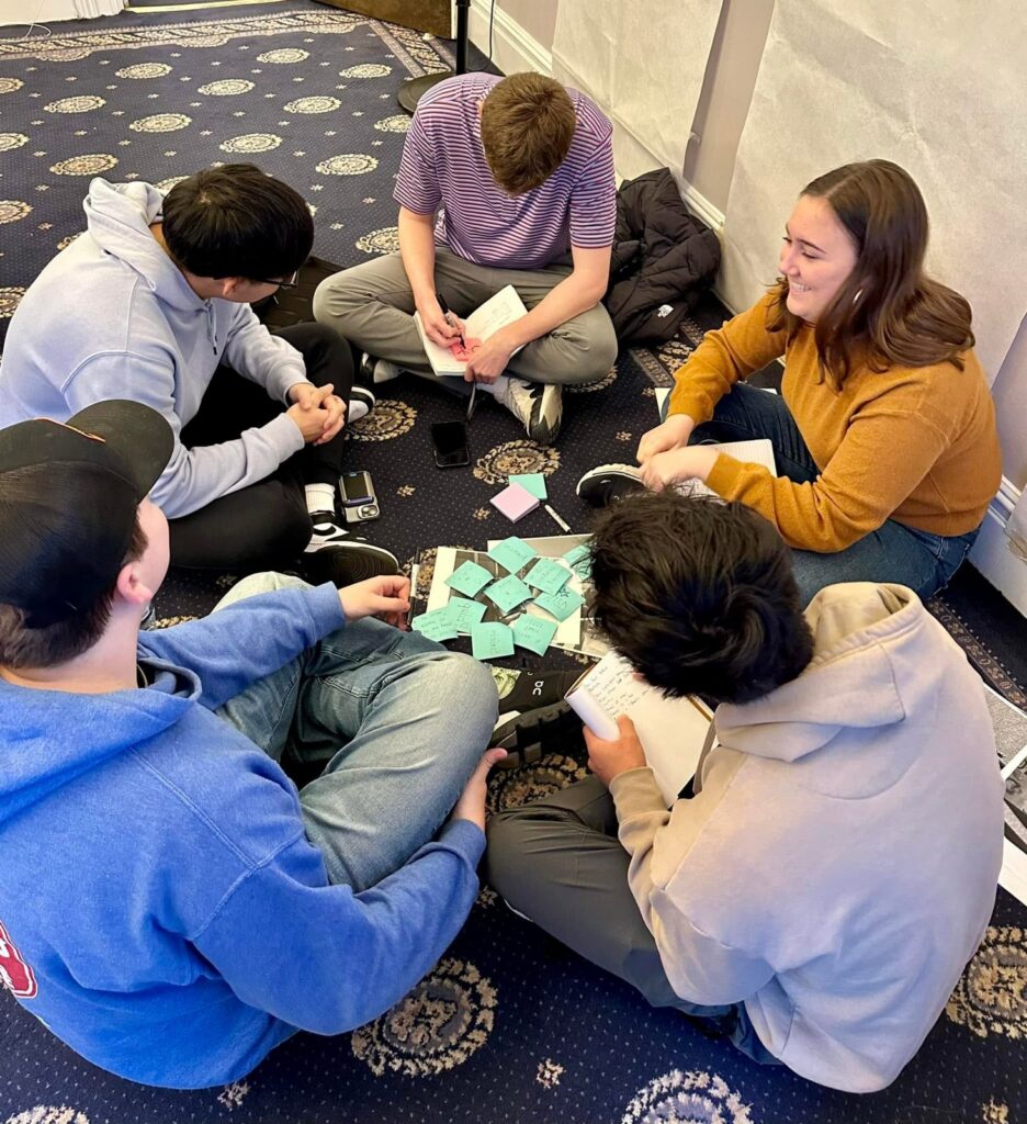 Students sit on the floor sharing interview stories around printed photos