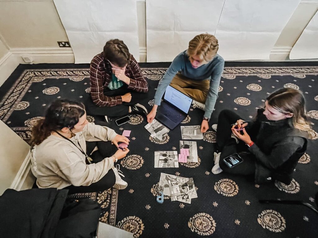 A student team sits on the floor sorting interview photos and notes