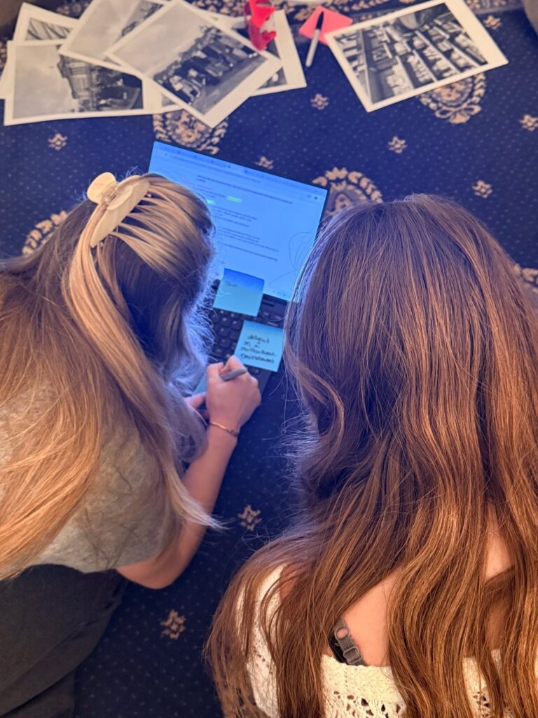 Overhead view of students reviewing printed photos and notes on a laptop