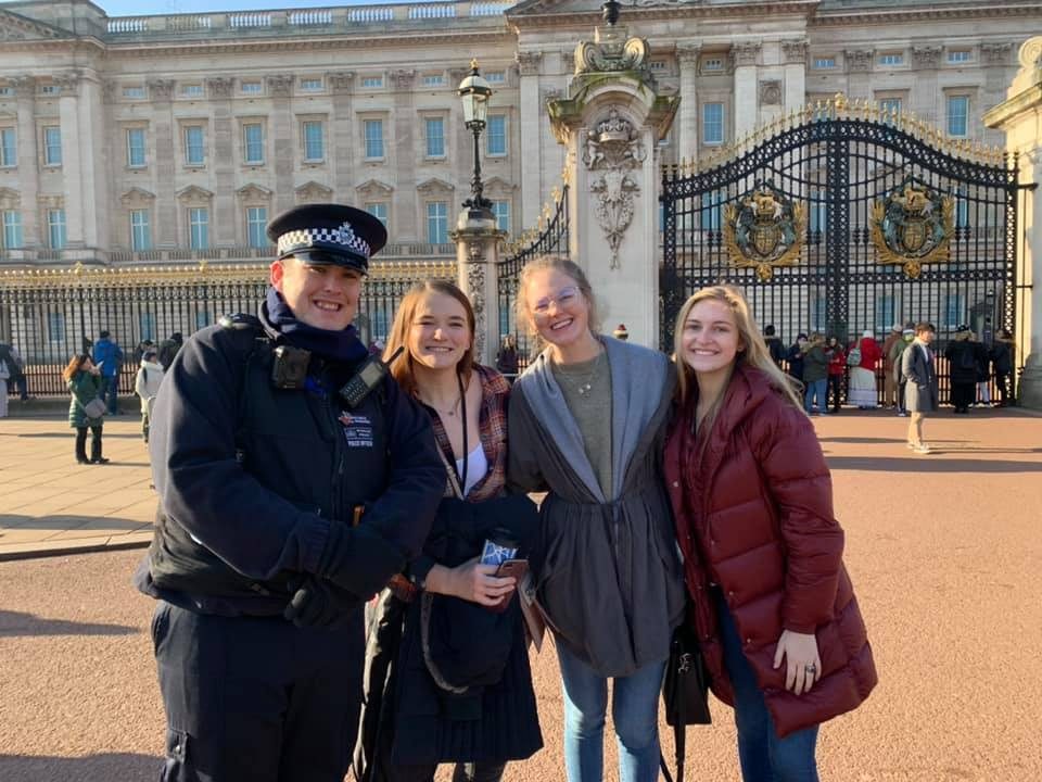 Students posing with a smiling London police officer outside Buckingham Palace after an interview
