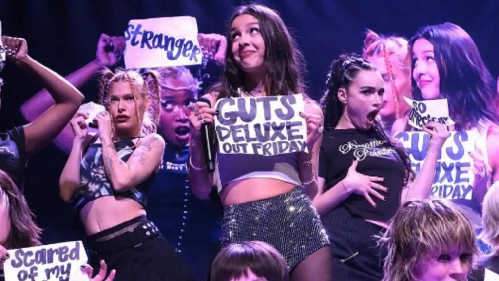 Olivia Rodrigo performing on stage in purple light during the GUTS tour