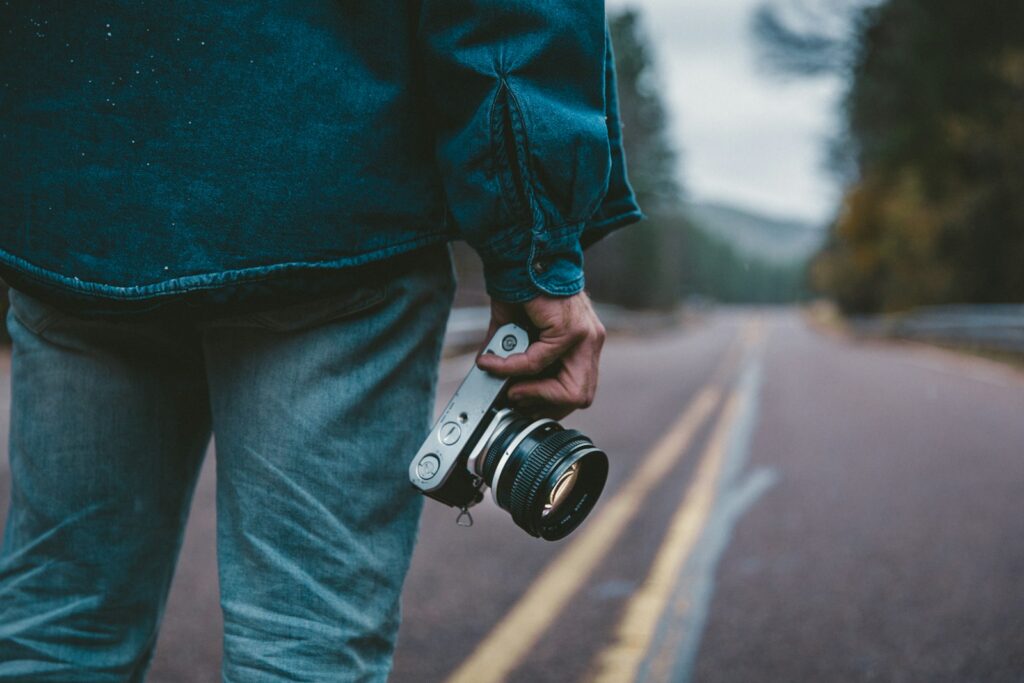 Person holding gray and black camera while standing on road