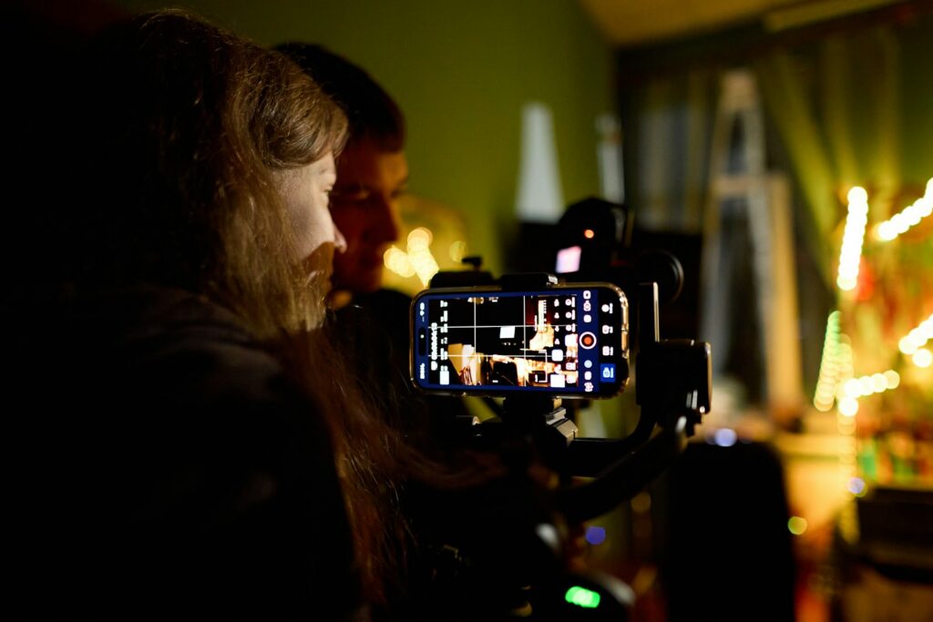 Two people filming with a smartphone mounted on a gimbal in a dim room